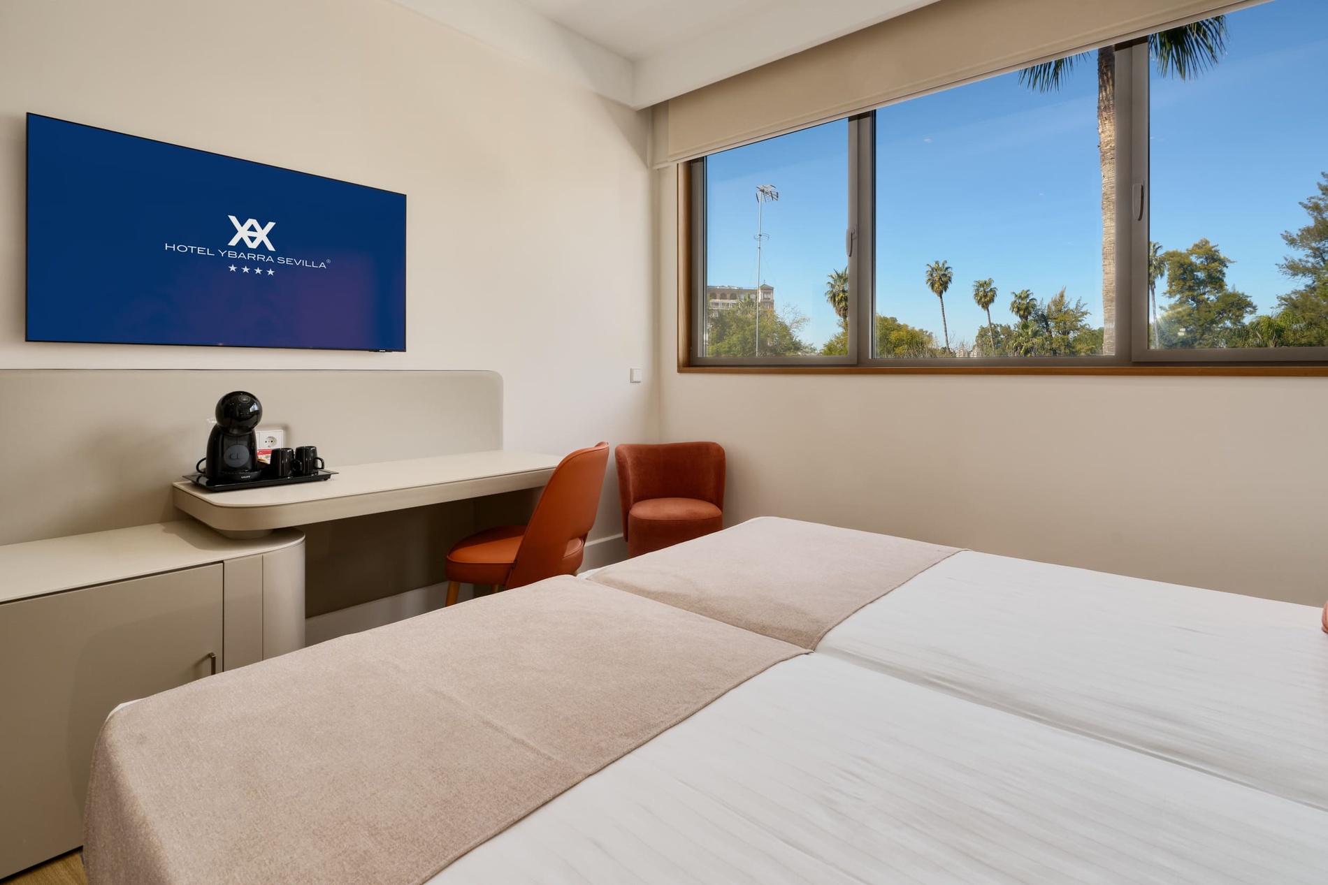 Modern hotel room at Ybarra Sevilla with twin beds and city view.
