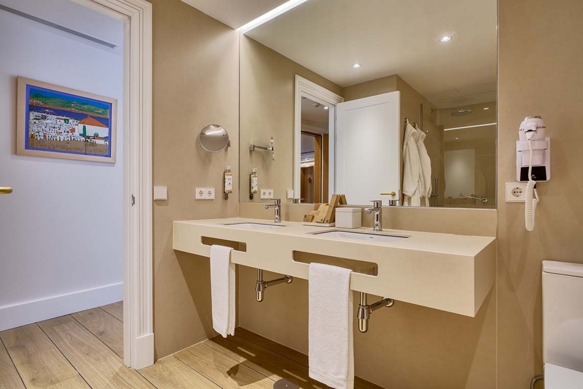 Un baño moderno y luminoso presenta un lavabo doble, un gran espejo y toques de madera, creando un ambiente cálido y funcional.