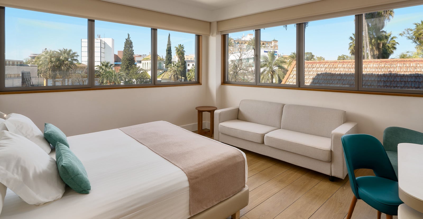 Una moderna y luminosa habitación de hotel con dos camas individuales juntas, papel tapiz de hojas de palmera, suelo de madera clara y muebles contemporáneos, incluyendo sillones de color naranja.