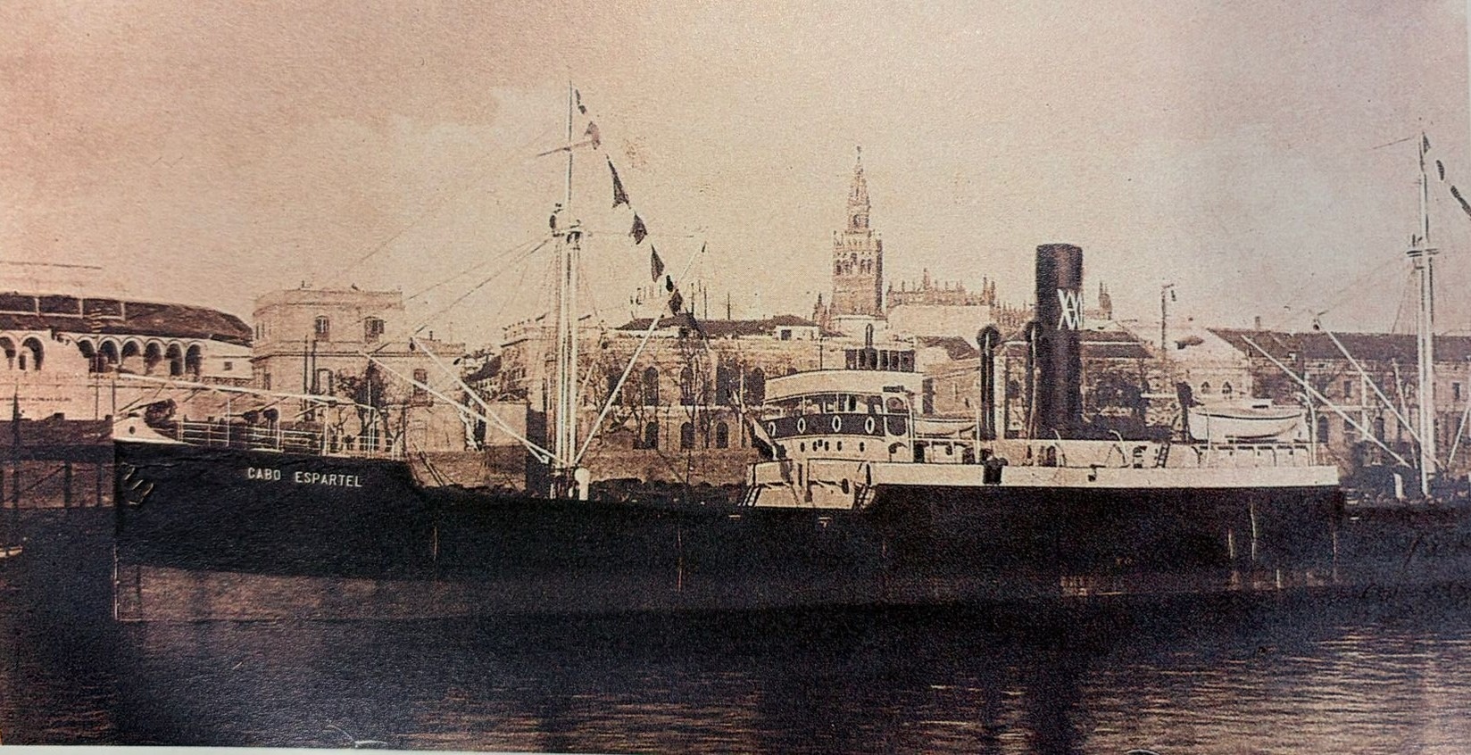Fotografía antigua en tono sepia del barco "Cabo Espartel" atracado en un muelle, con la Giralda de Sevilla destacando al fondo.