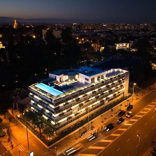 Modern Ybarra Sevilla hotel with rooftop pool illuminated at dusk.