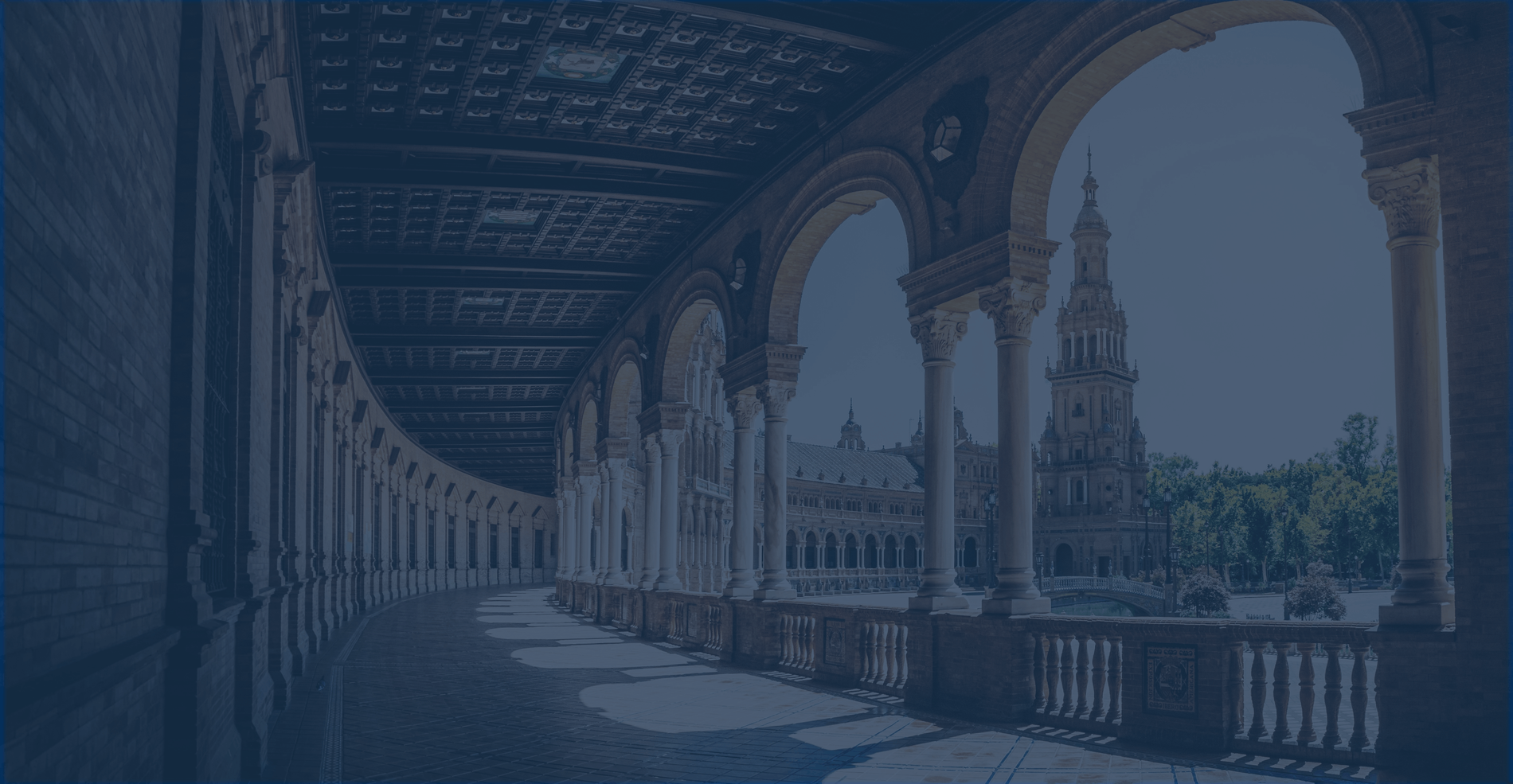 un edificio de ladrillo con columnas y arcos y una iglesia en el fondo=s1900