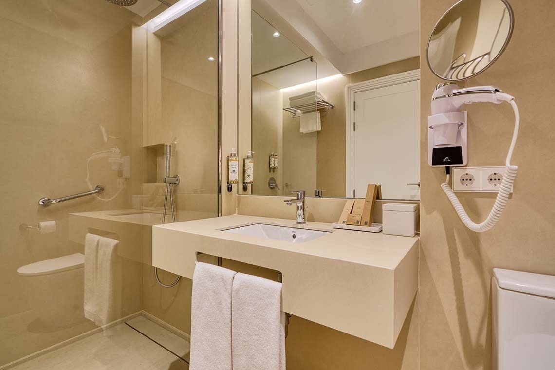 Un moderno y luminoso baño en tonos crema, equipado con ducha acristalada, lavabo, inodoro y secador de pelo.