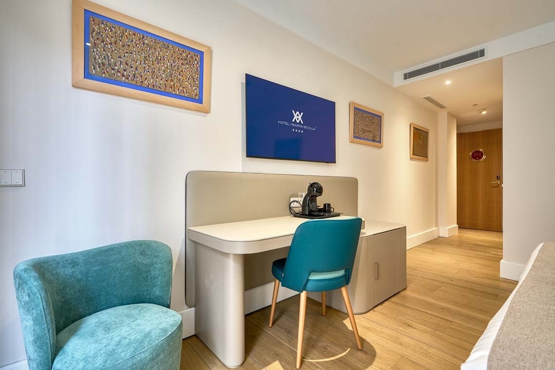 Una moderna habitación de hotel presenta un escritorio con silla, un televisor en la pared, un sillón y varias obras de arte.