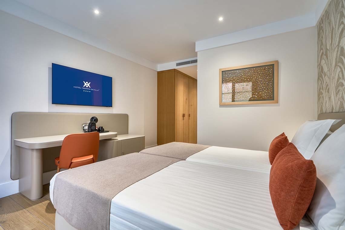 Esta moderna habitación de hotel cuenta con camas gemelas, un escritorio con cafetera y un televisor montado en la pared.