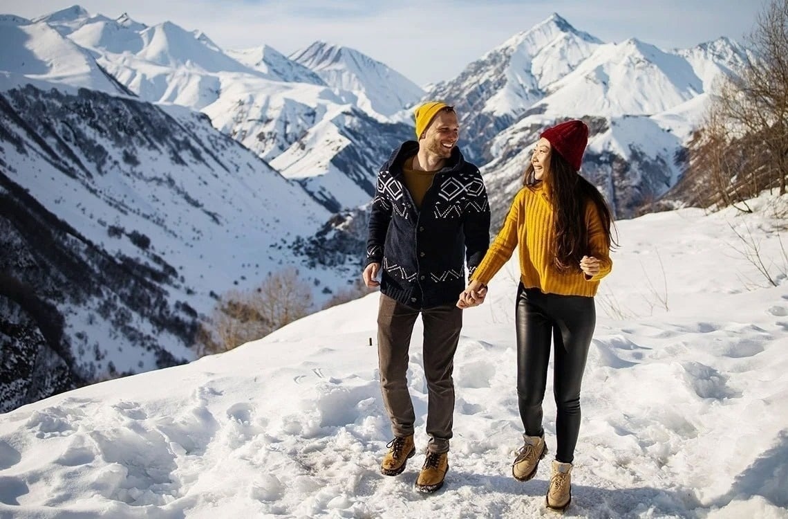 un hombre y una mujer sostienen las manos mientras caminan por la nieve