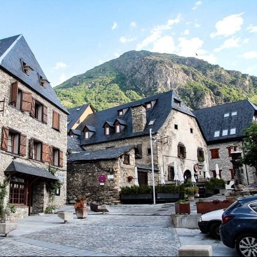 une petite place avec des maisons en pierre et des voitures garées