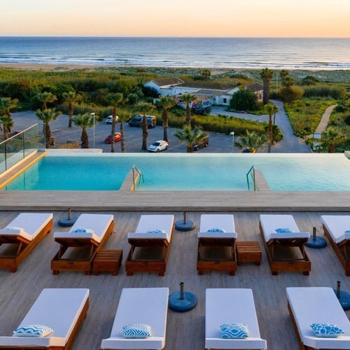 Liegestühle stehen neben einem Infinity-Pool mit Blick auf den Ozean