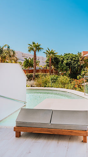 Modern lounge chair by a private pool with palm trees and resort buildings, perfect for your Qhotels: Zahara Beach & SPA.