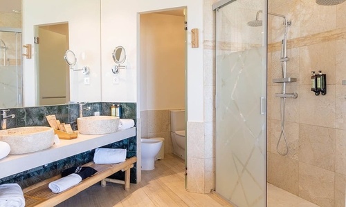 Ein modernes Badezimmer ist mit Doppelwaschbecken aus Naturstein, einer begehbaren Dusche und einem separaten Toilettenbereich ausgestattet.