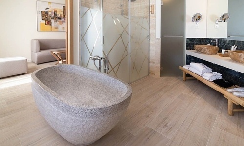 Ein modernes Badezimmer mit großer Steinbadewanne, einer Duschkabine mit gemusterten Glaswänden und einem Doppelwaschbecken grenzt an einen Wohnbereich mit Sofa.