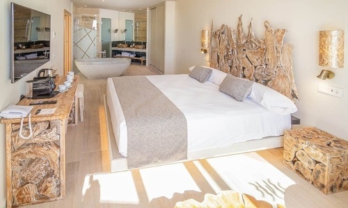 Dieses stilvolle Hotelzimmer verfügt über ein großes Bett, einen offenen Badbereich mit freistehender Badewanne und rustikale Möbel aus Naturholz.