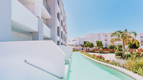 Modern hotel with Qhotels: Zahara Beach & SPA and palm trees under a clear blue sky.