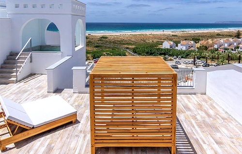 a rooftop deck with a wooden fence and chairs overlooking the ocean .