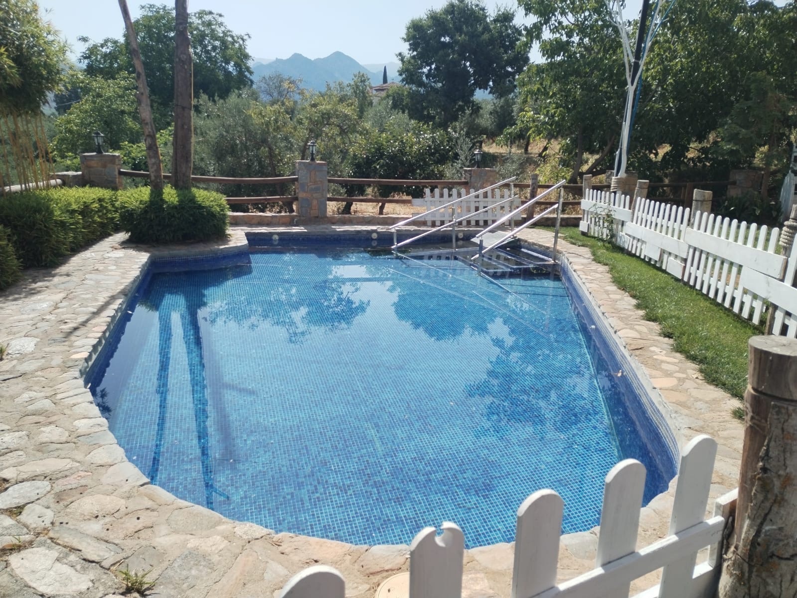 una piscina rodeada de árboles y una valla blanca