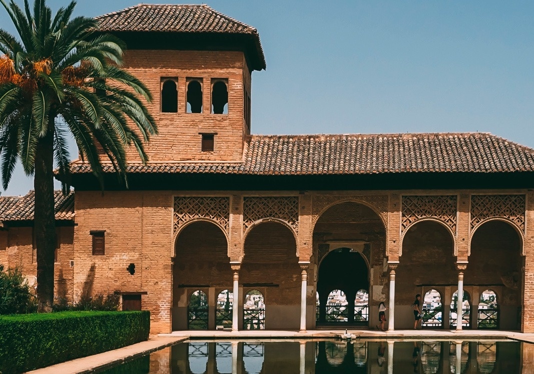 un edificio de ladrillo con una piscina y palmeras en el fondo