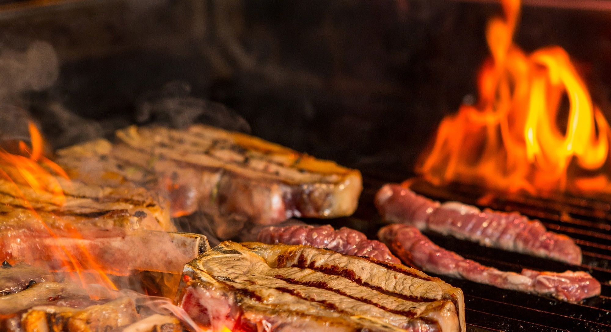 una parrilla llena de carne y fuego en el fondo