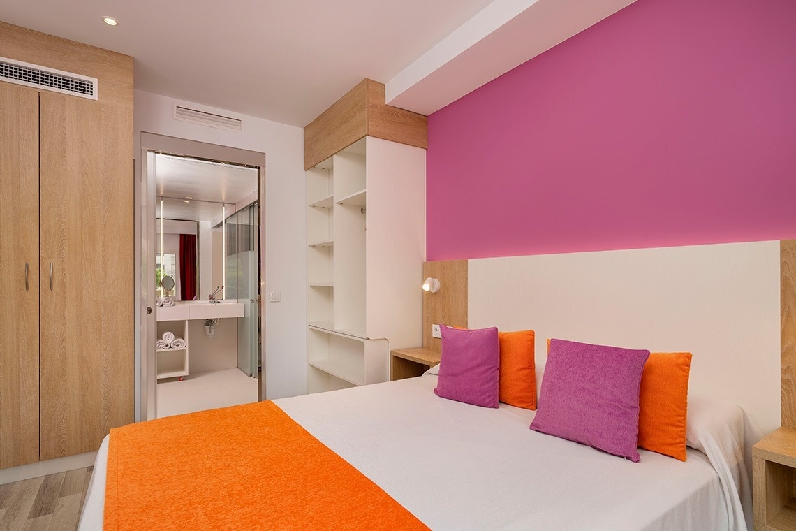 a bedroom with a pink wall and a bed with orange and purple pillows