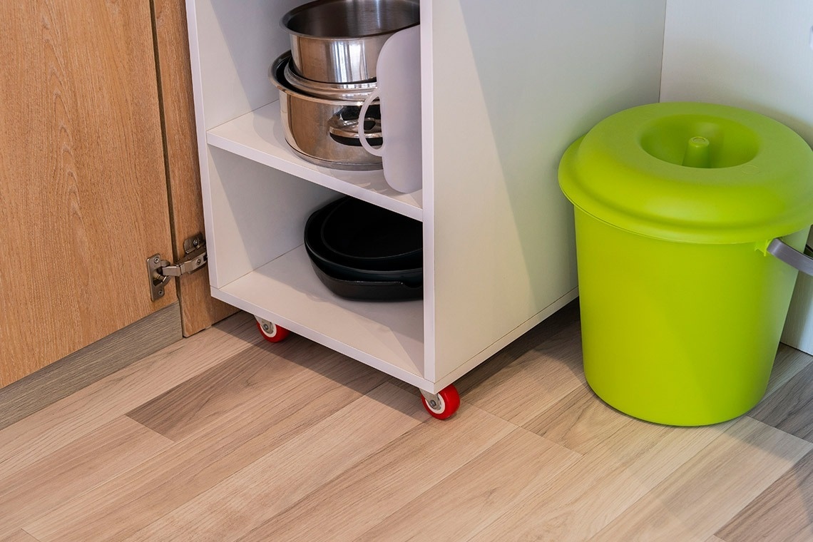 a green trash can sits next to a shelf with pots and pans on it