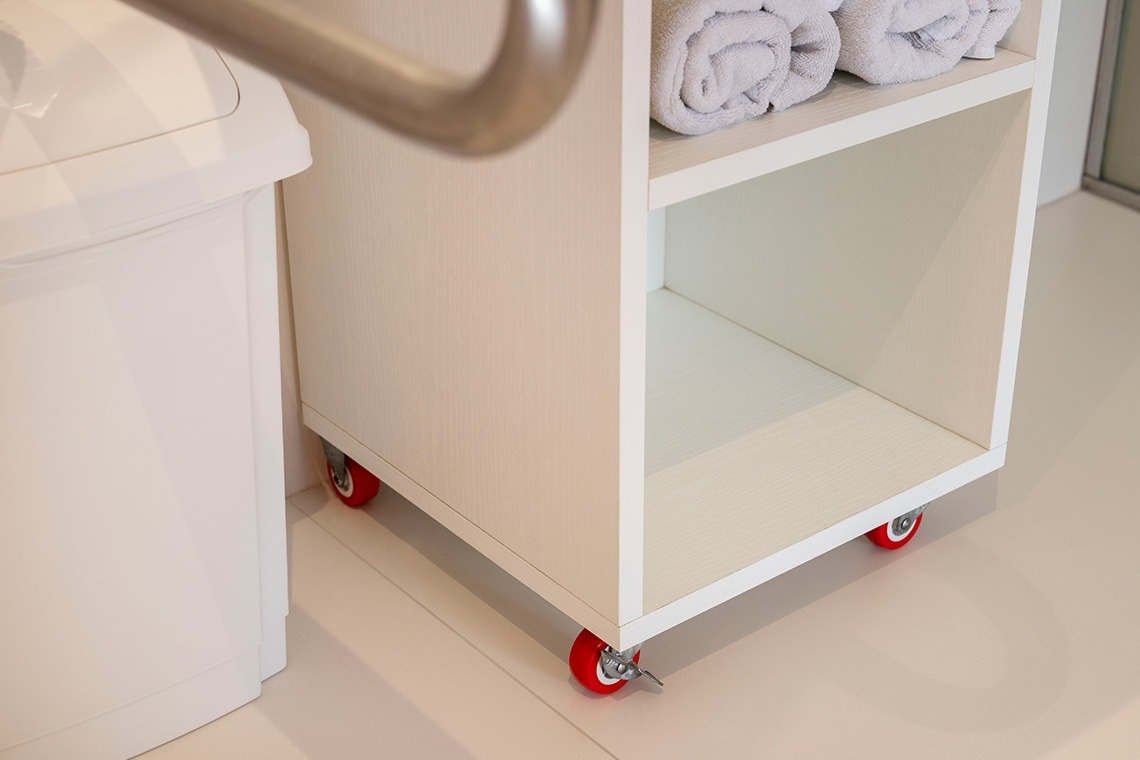 a white shelf with red wheels has towels on it