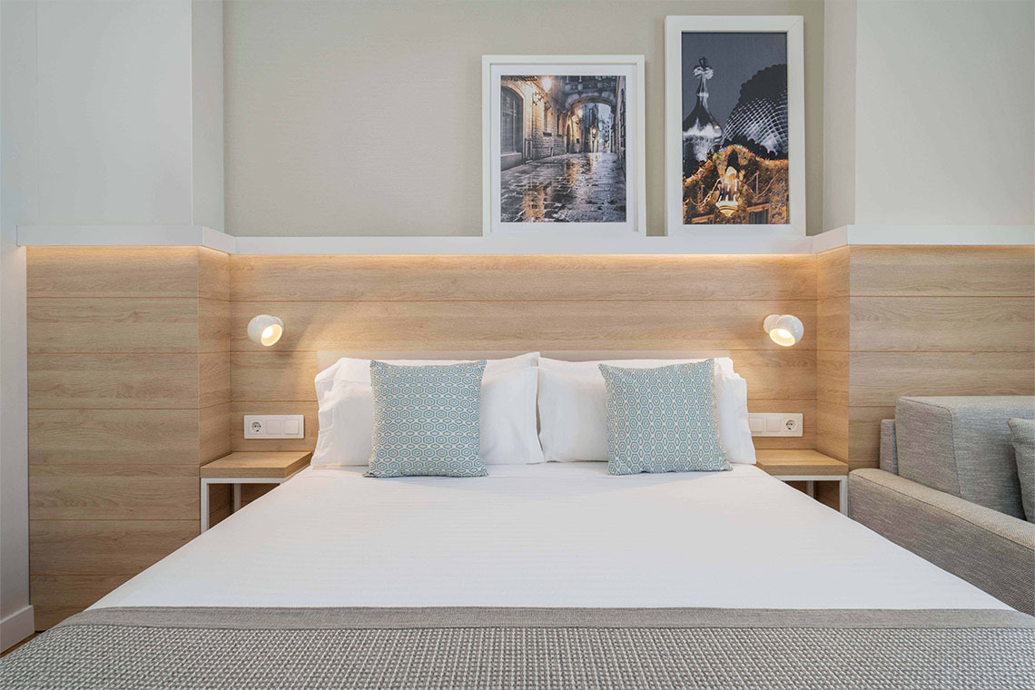 Dettaglio del letto matrimoniale, testiera in legno e illuminazione nella Camera Classic 1 Letto di ZT The Golden Barcelona Hotel.