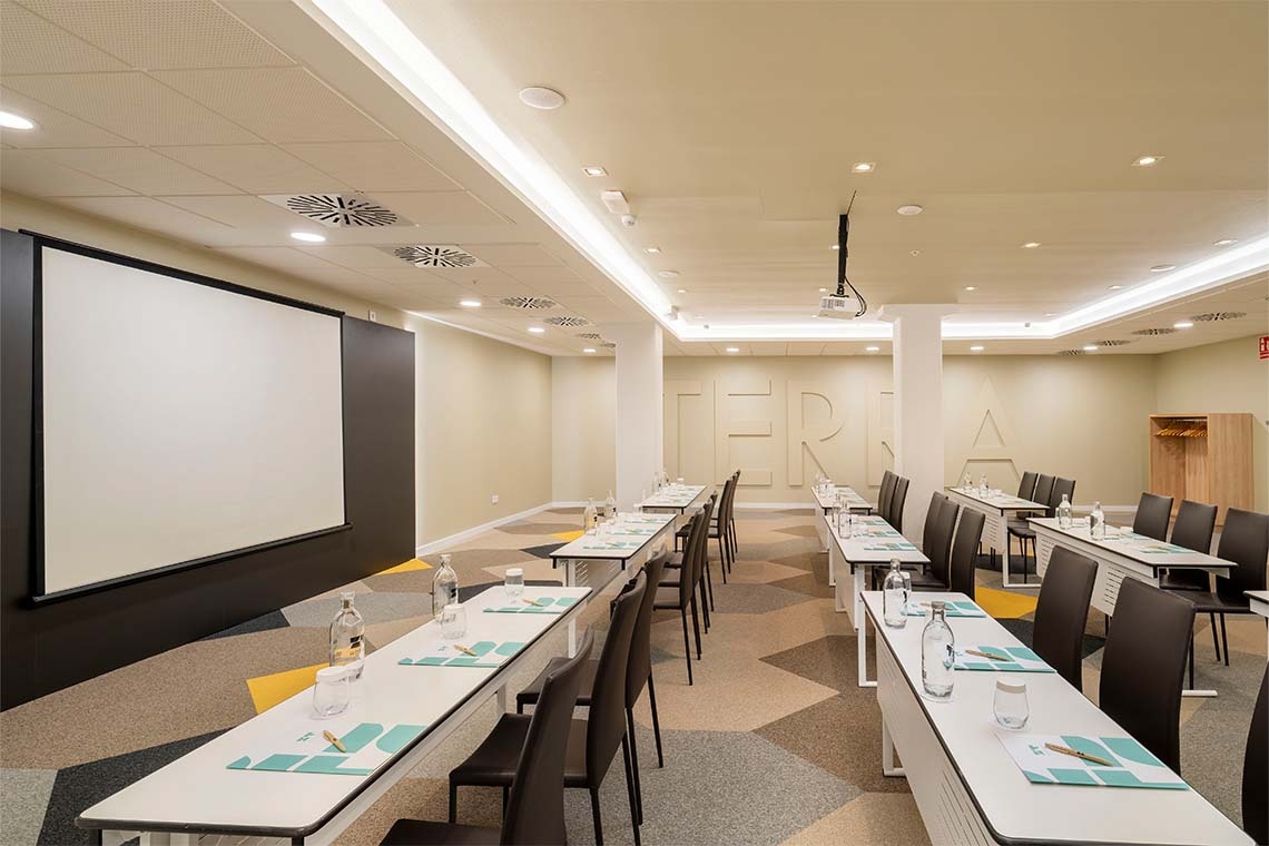 Golden Barcelona conference room with presentation screen, tables, and chairs set up for a meeting.