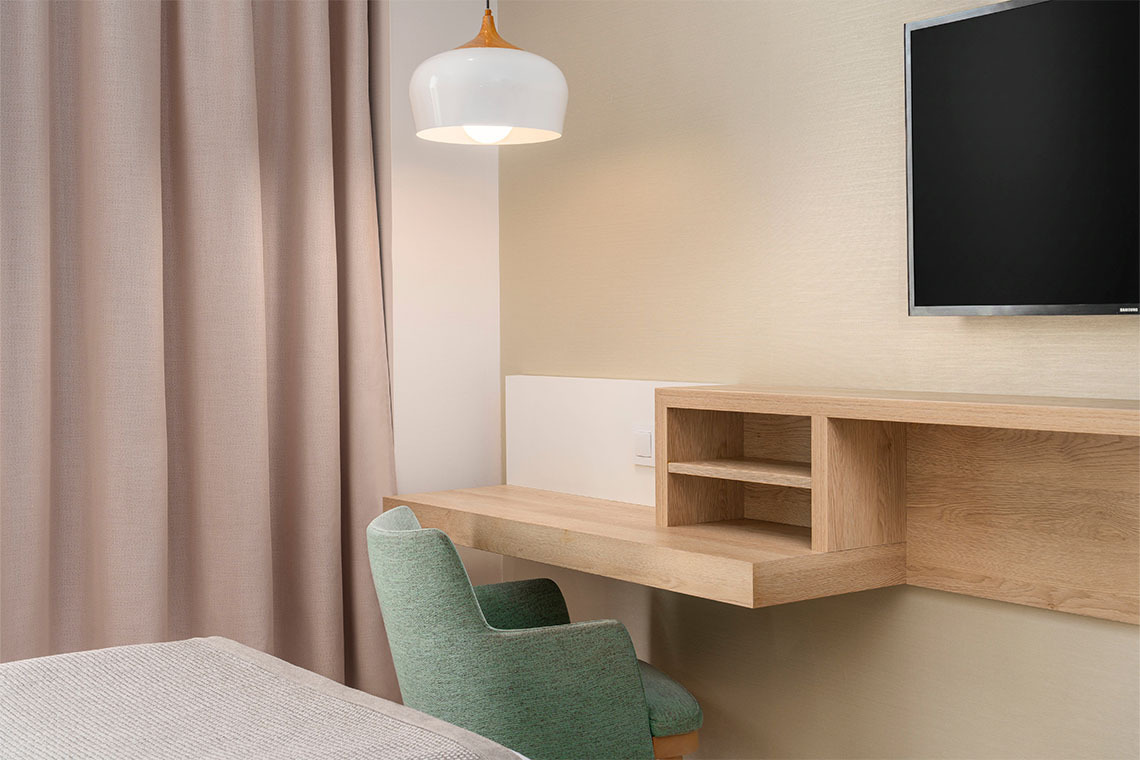Escritorio de madera en habitación de hotel, con silla verde y lámpara colgante. ZT: Golden Barcelona