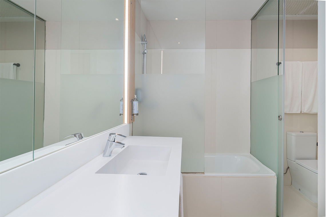 Bagno moderno con lavabo, vasca e WC separati da pareti in vetro.
