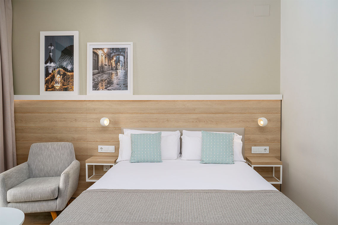ZT: Golden Barcelona: cama doble con cojines decorativos y sillón gris en una habitación de hotel.
