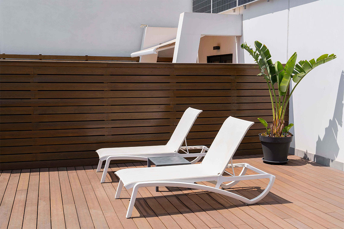 Lounge chairs and plant on a modern wooden deck with a sleek white building.