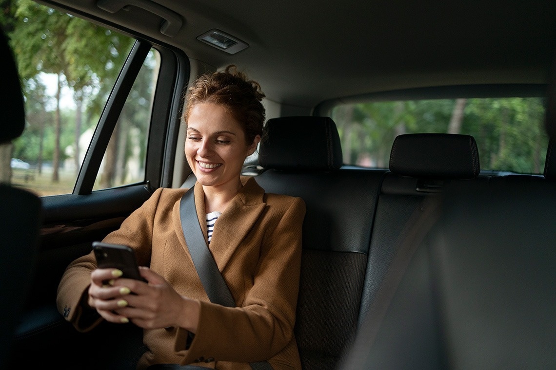 una mujer está sentada en el asiento trasero de un automóvil mirando su teléfono celular