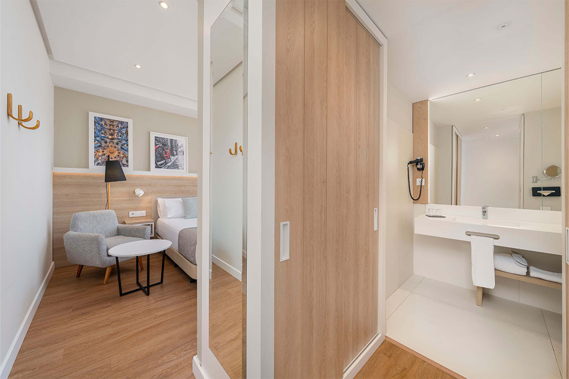 Camera di hotel moderna con letto, poltrona, specchio e bagno con lavabo.