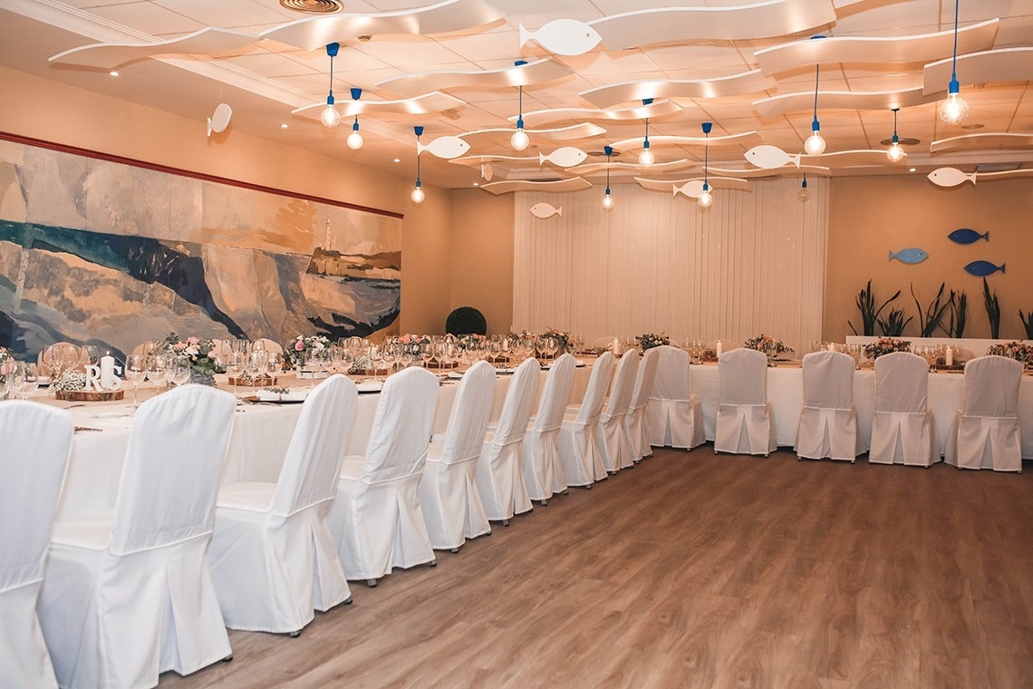 una larga mesa y sillas blancas en una habitación con peces colgando del techo