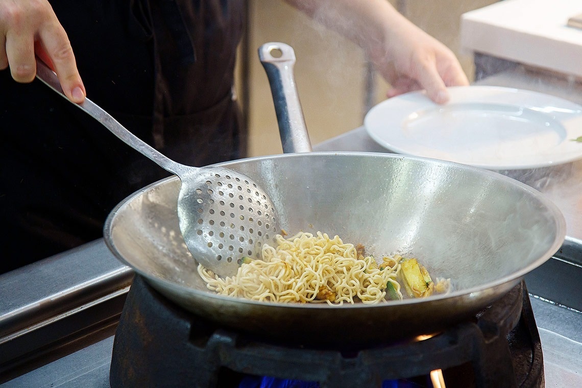 una persona está cocinando fideos en una sartén en una cocina
