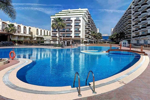 Piscina exterior de Peniscola Plaza Suites con puentes de madera y tumbonas.