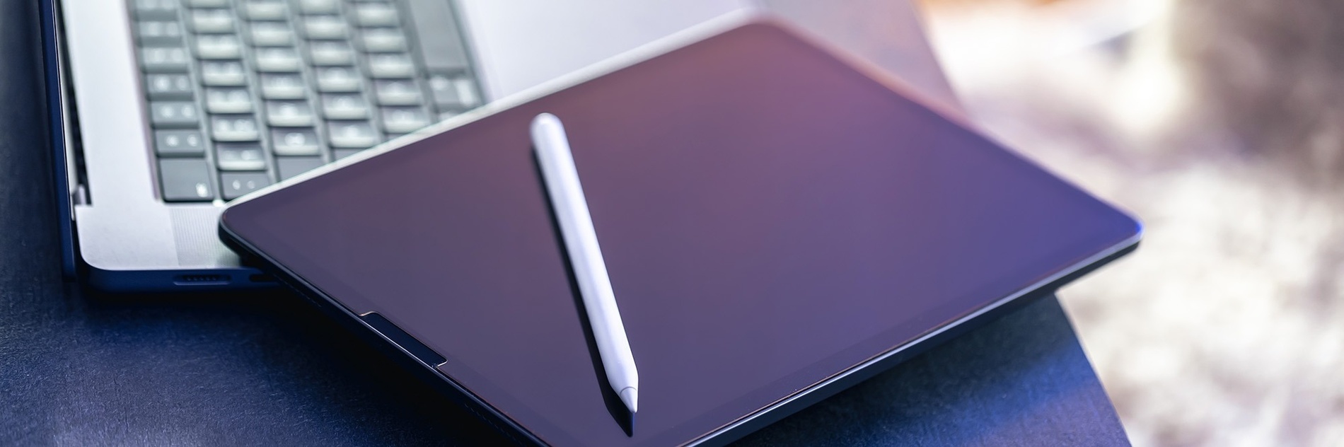 una tableta y un lápiz están sobre una mesa junto a una computadora portátil