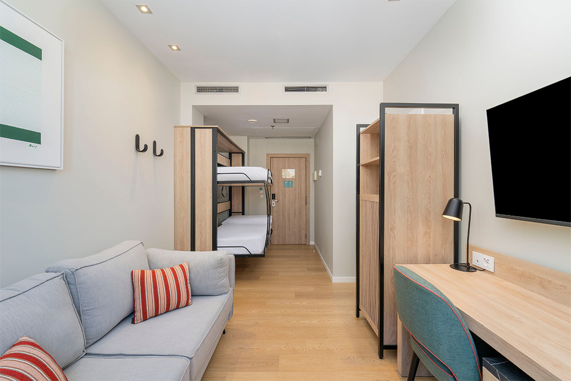 Habitación familiar moderna con literas, sofá y escritorio en hotel, ideal para ZT: Villa Olimpica.