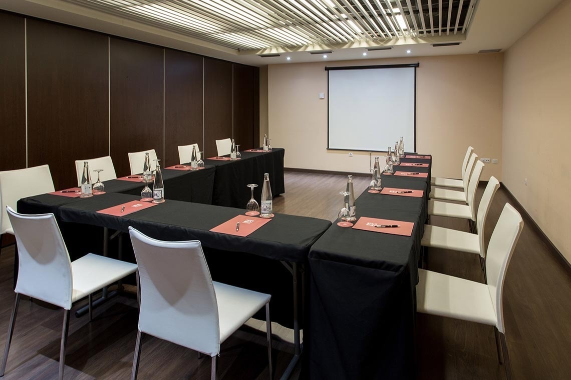 una sala de conferencias con mesas y sillas y una pantalla de proyección