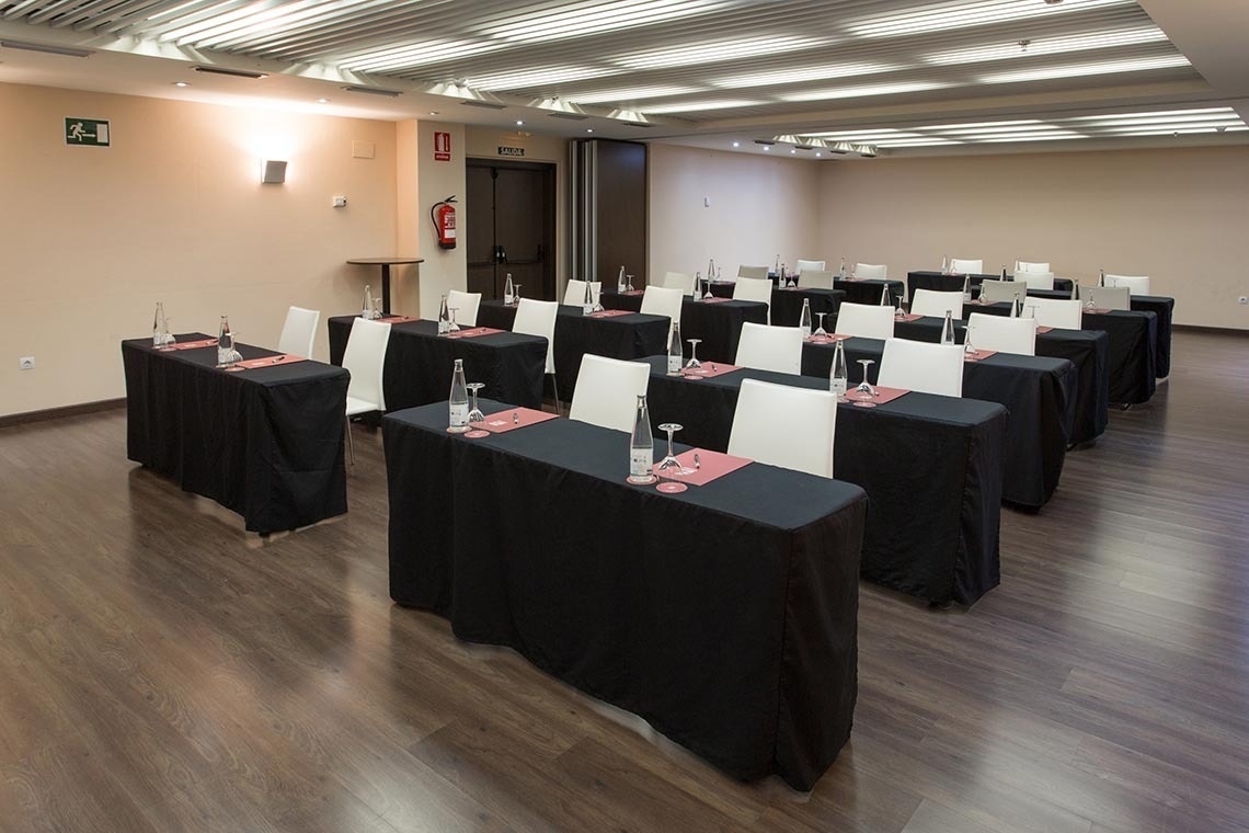 una sala de conferencias con mesas negras y sillas blancas