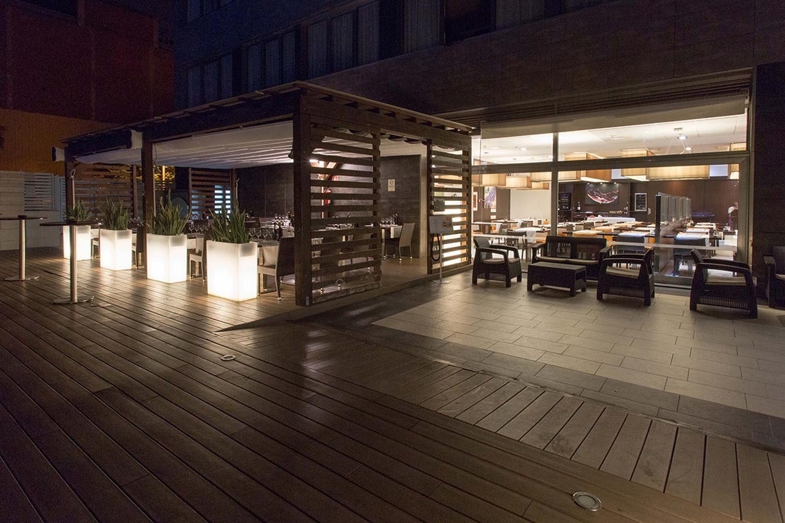 una terraza de madera con mesas y sillas al fondo