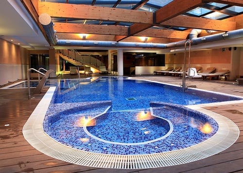 una persona sostiene un cóctel frente a una piscina infinita