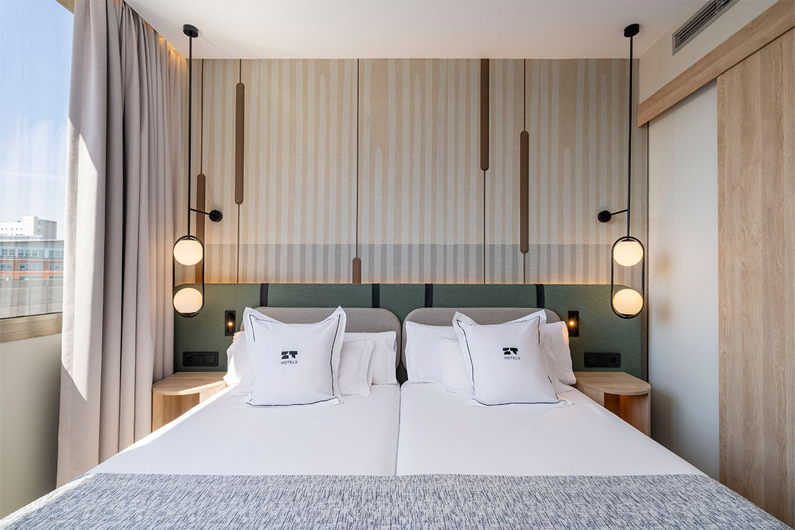 Habitación doble moderna con dos camas, almohadas con ZT: Villa Olimpica y lámparas colgantes.