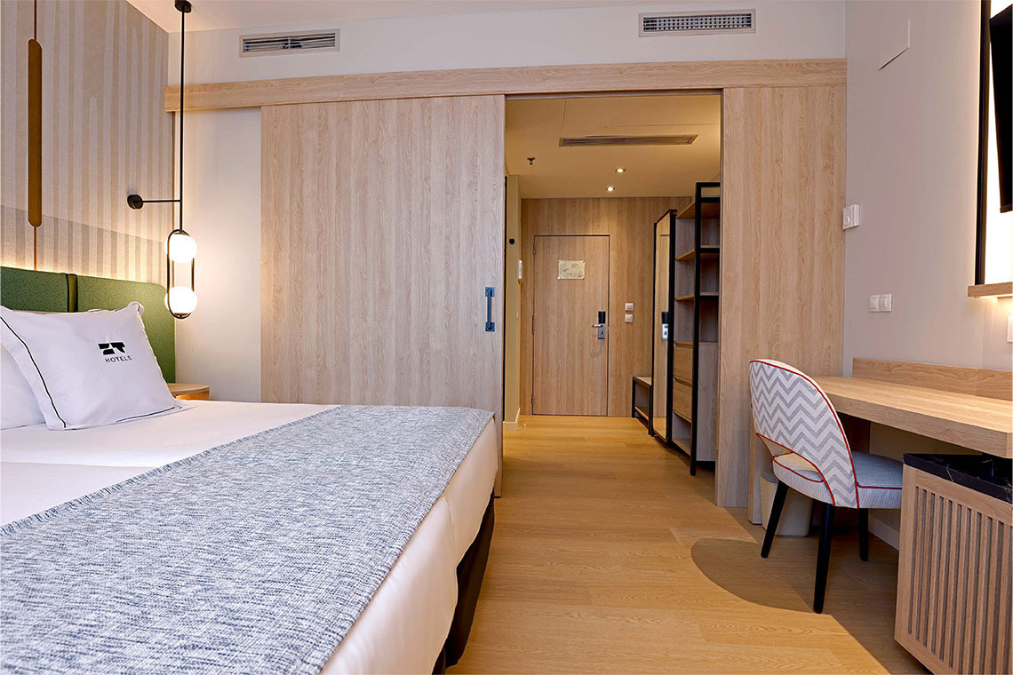 Habitación de hotel moderna con cama, escritorio, silla y puerta corredera. ZT: Villa Olimpica