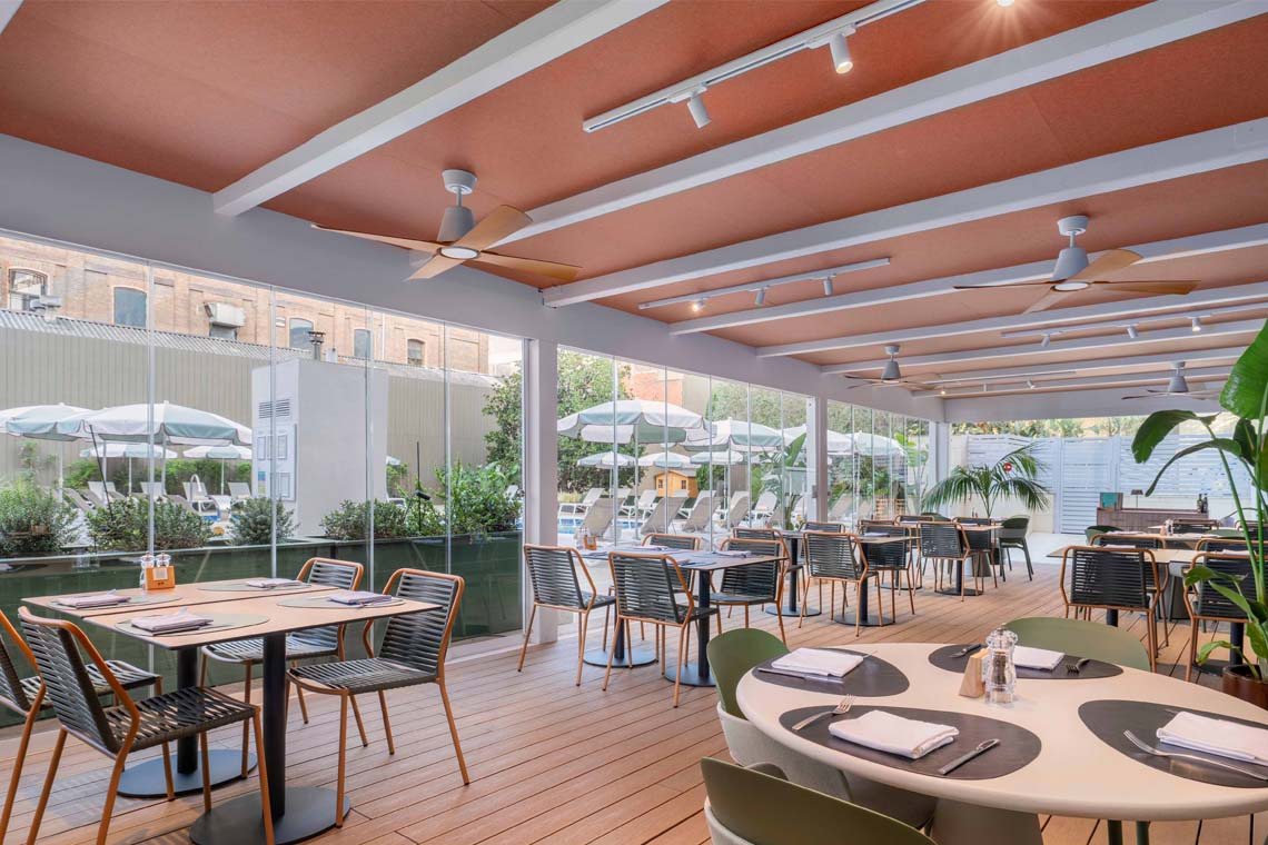 Terraza de restaurante con mesas y sillas al aire libre, junto a la piscina de ZT: Villa Olímpica.