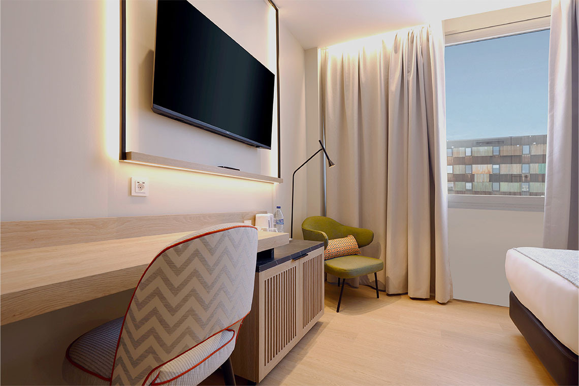 Habitación moderna con escritorio, TV, silla verde y ventana. ZT: Villa Olimpica